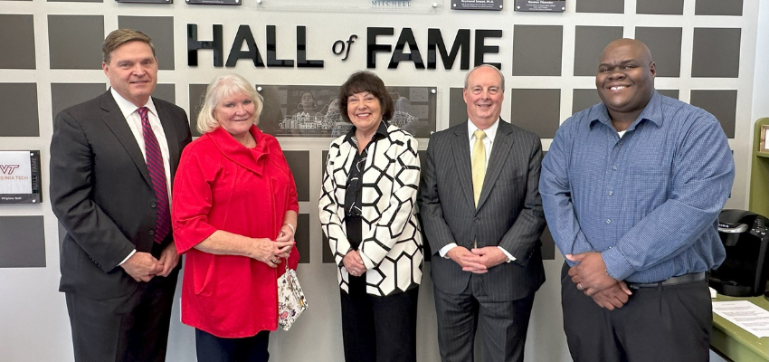 A group of five individuals stands, including Dr. Tookes-Rawlins, in front of a 'Hall of Fame' wall. They are all dressed in formal attire, smiling for the camera.
