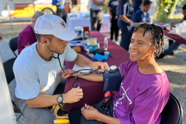 A healthcare worker checks a smiling woman's blood pressure outdoors at a community health event.
