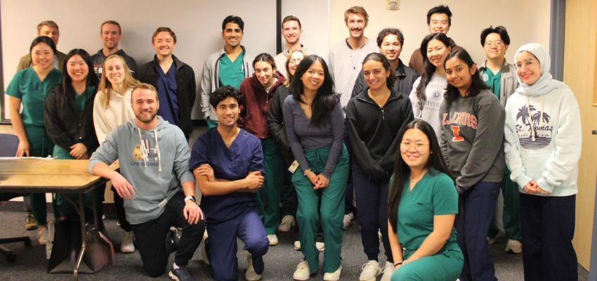 A group of smiling medical students poses together in a classroom setting.