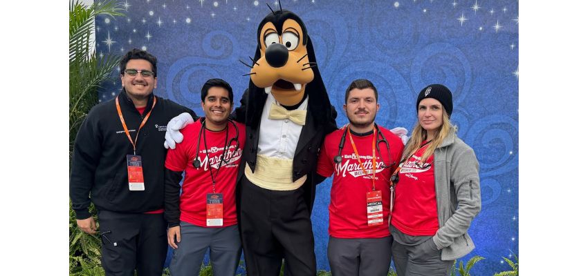 A group of individuals wearing red shirts stands with Goofy in a fun outdoor setting.