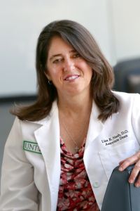 A woman in a white coat, identified as an associate dean, smiles while seated at a table.