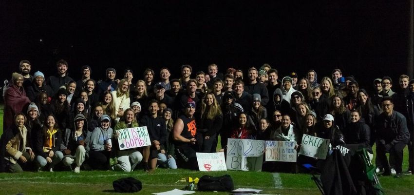 A large group of students gathers outdoors at night, holding supportive and celebratory signs.