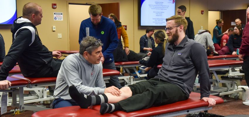 A group of medical professionals practices techniques on treatment tables in a hands-on workshop setting.