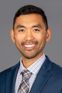 A professionally dressed man smiles in a headshot portrait against a neutral background.