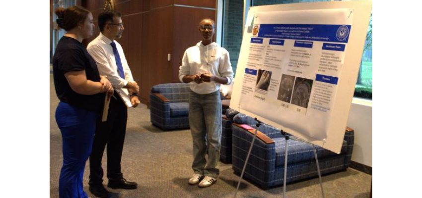 A student at the Chicago College of Osteopathic Medicine (CCOM) presents a research poster to two attendees in an indoor setting with lounge seating.