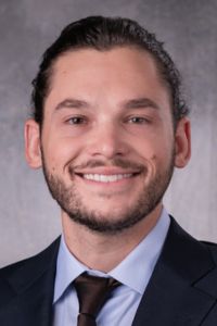 A professional headshot of a smiling man in a suit, representing a student or faculty member from CHSU-COM.