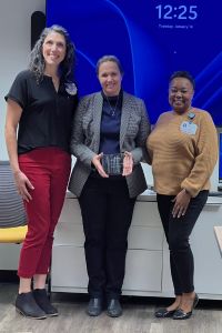 Three women stand together in a professional setting at the University of North Texas Health Science Center - Texas College of Osteopathic Medicine (UNTHSC-TCOM), one holding an award or plaque.