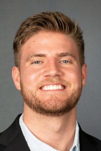 A headshot of a smiling man in professional attire against a neutral background.