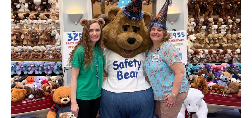 Two women pose with a person in a bear mascot costume wearing a 