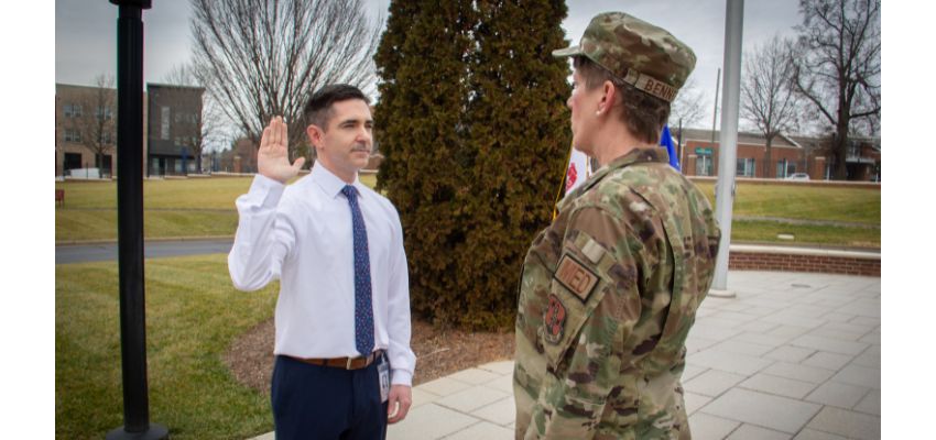 A man in a white shirt raises his right hand while taking an oath in front of a uniformed military officer.