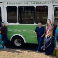 AgroupofmedicalstudentsinscrubsposesinfrontofaSummerVillageassistedlivingfacilityshuttlebus