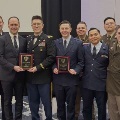 Agroupofmilitaryservicemembersandstudentsindressuniformsposetogetheratanawardsceremonywithtwoindividualsholdingplaques