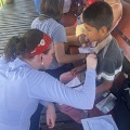 Amedicalvolunteerwearingaredbandanaexaminesayoungboysthroatatanoutdoorcommunityhealthevent