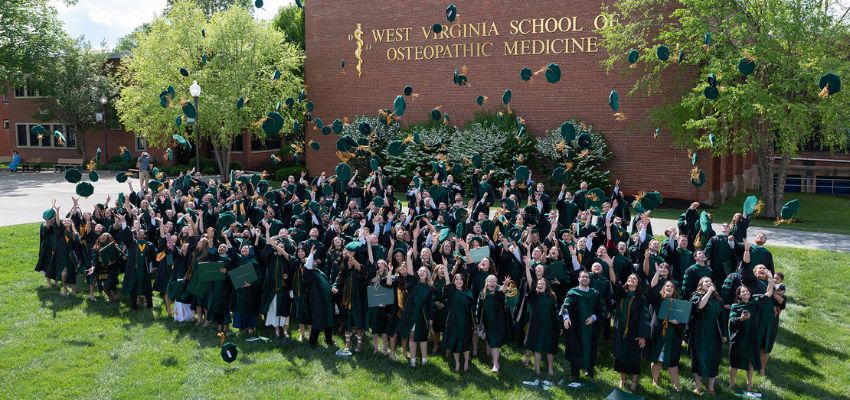 Graduates from the West Virginia School of Osteopathic Medicine celebrate by tossing their caps in the air outside the school building.