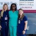 ThreewomeninmedicalscrubsstandsmilinginfrontofaVCOMLouisianamobileclinicvehicle