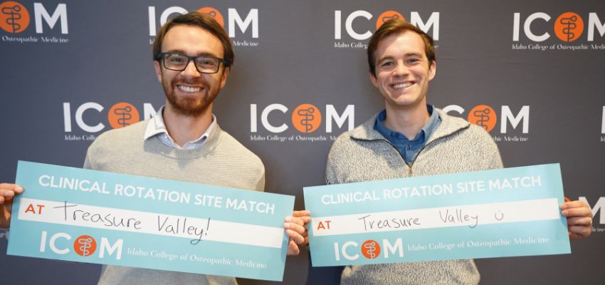 Two students smile while holding signs announcing their clinical rotation site match at Idaho College of Osteopathic Medicine.