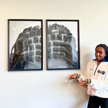 Abigail smiles, standing next to her framed photos