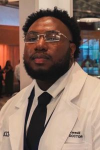 John Okwesili standing in OCOM foyer in white coat