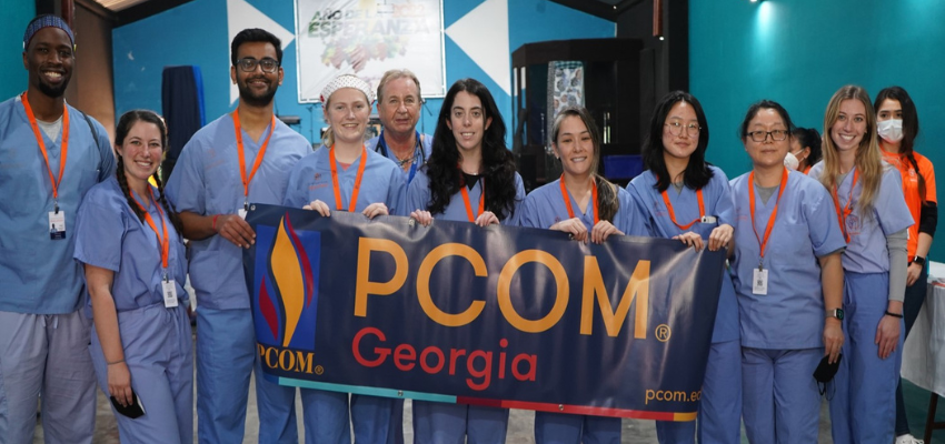 Students hold PCOM Georgia banner in clinic.