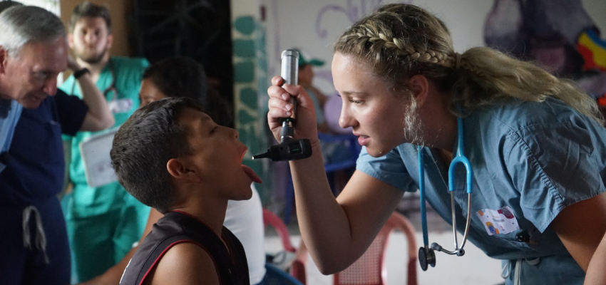 Student looks into child's mouth using otoscope.