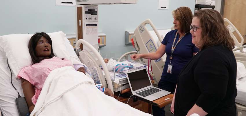 Two faculty members look towards manikin