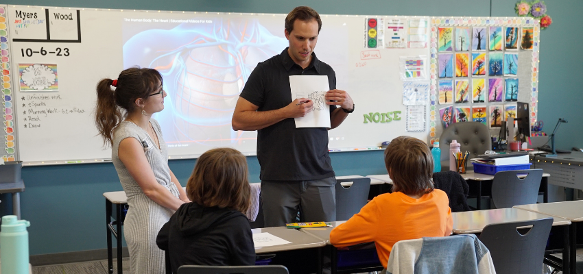 Medical students hold up diagram of human heart in an elementary school classroom