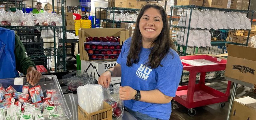 Student smiles while packing apples into a plastic bag.