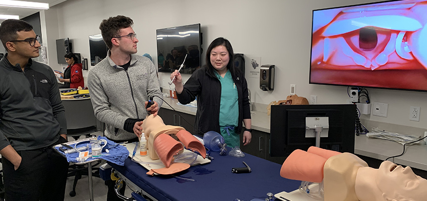 Des Moines University graduate Anh Tang, DO (right), an internal medicine resident at MercyOne in Central Iowa, guides students in intubating a medical mannequin in the university’s surgery/simulation lab.