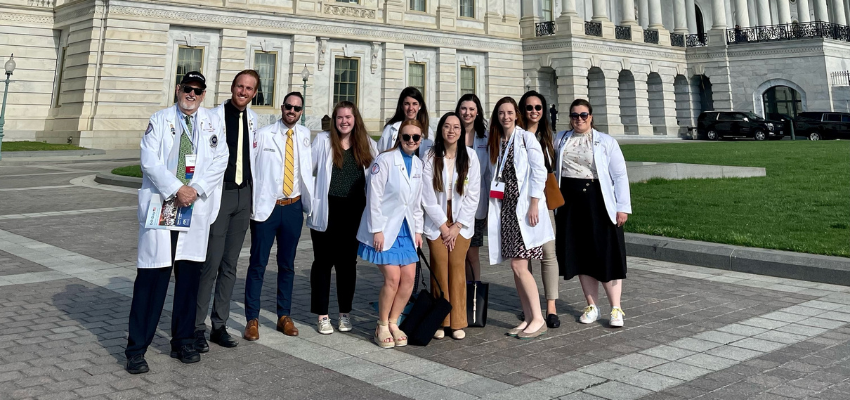 Students in white coats stand in front of US Capitol.