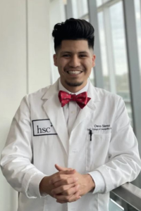 A student from the University of North Texas Health Science Center Texas College of Osteopathic Medicine poses indoors, wearing a white coat and a red bow tie, with a broad smile.