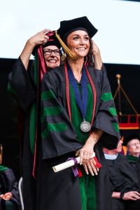  graduate in a cap and gown receiving their diploma on stage during a commencement ceremony.