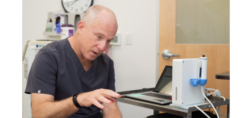 A medical professional in navy scrubs demonstrating the use of a medical device during a clinical setting.