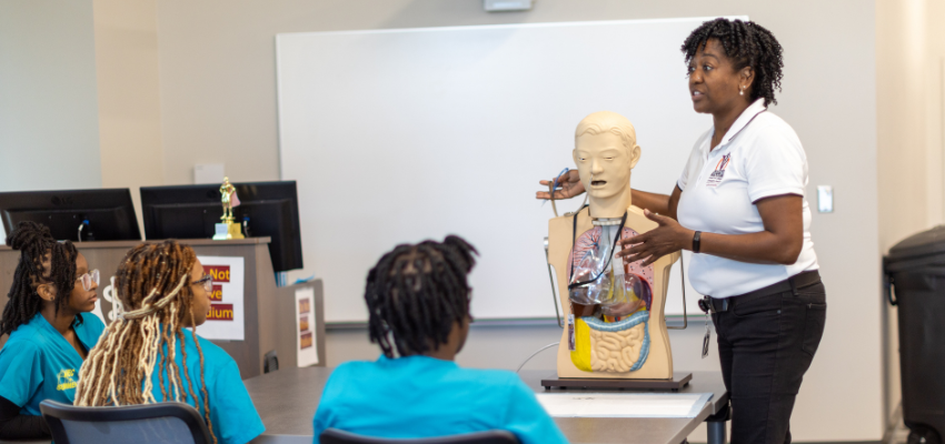 An instructor demonstrating a medical mannequin to a group of students in a classroom.