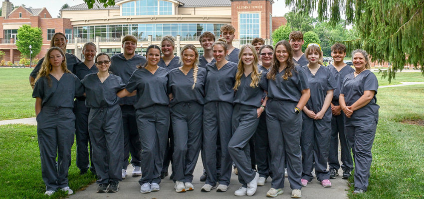 Students in medical scrubs stand on campus lawn