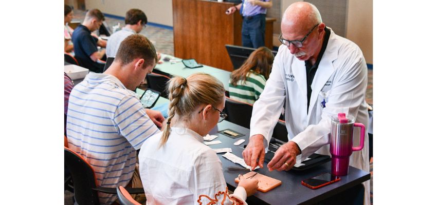 A medical instructor guiding a student in a hands-on suturing workshop.