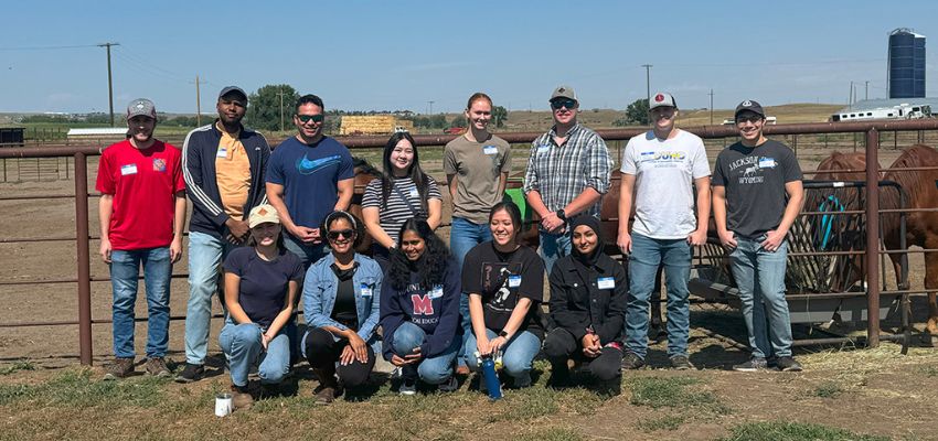 A group of medical students pose together outdoors in front of a horse corral during a community event.