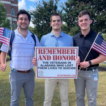 Three medical students hold a sign honoring veterans who lost their lives to suicide.