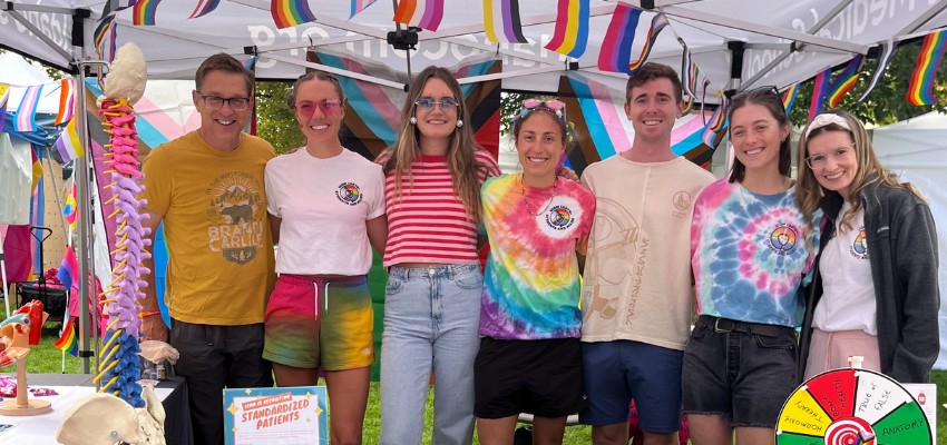 Group of students wearing colorful outfits and standing together at a pride event booth.