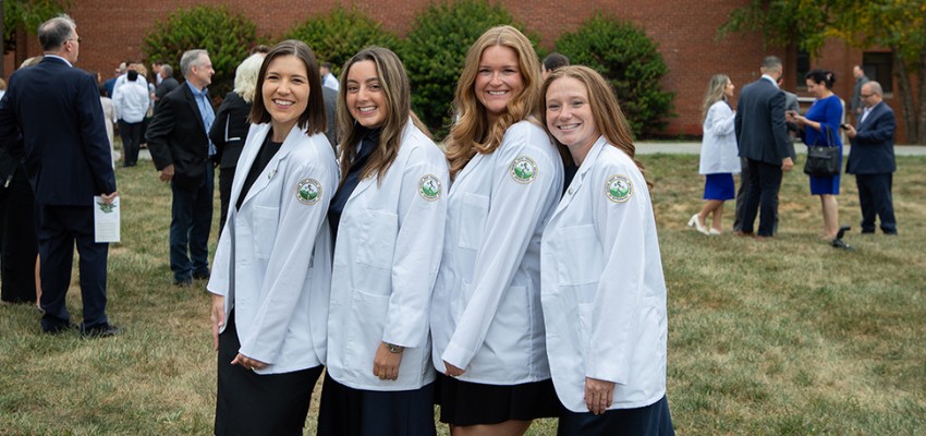 Group of four medical students smiling outdoors in white coats.