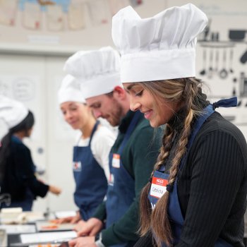 Students in chef hats and aprons participating in a cooking class, focusing on food preparation.