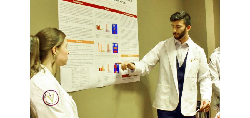 A medical student presenting research findings using a poster, explaining details to another student.