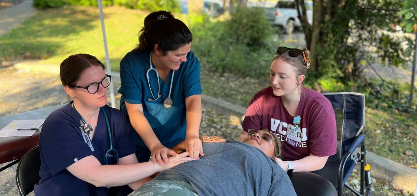 A group of healthcare workers and medical students providing hands-on care to a patient during a clinical exercise outdoors.