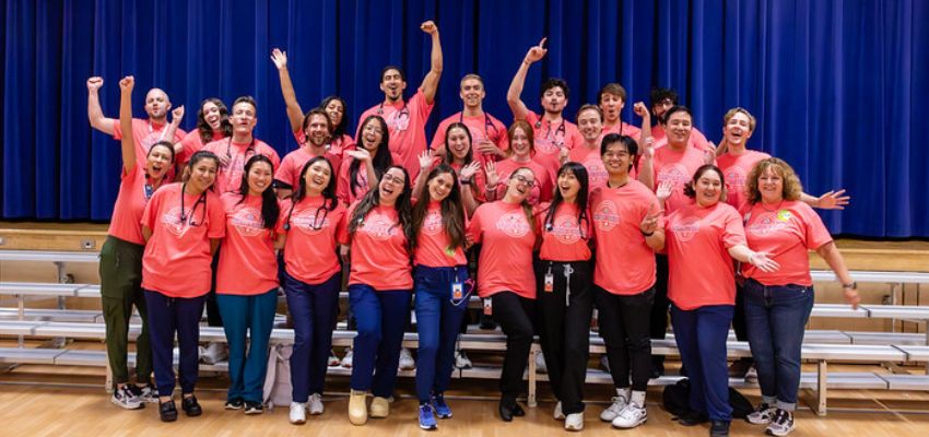 A group of medical students enthusiastically posing in matching pink shirts for a group photo.