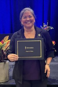 A smiling woman proudly holding a certificate on stage, signifying her achievement at a professional event.