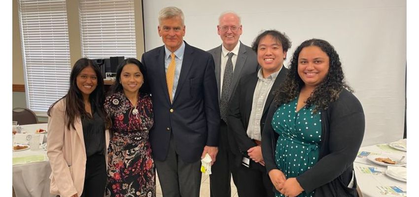 A group of attendees poses with a distinguished guest at a formal event.