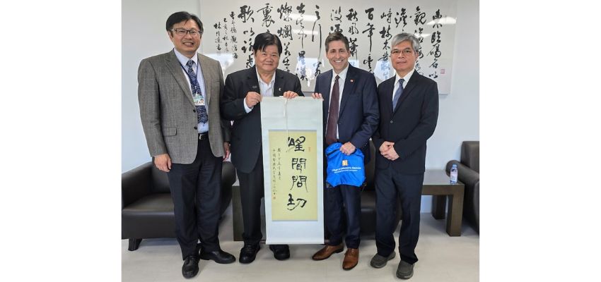 Four professionals posing with a scroll featuring traditional calligraphy during an official exchange.