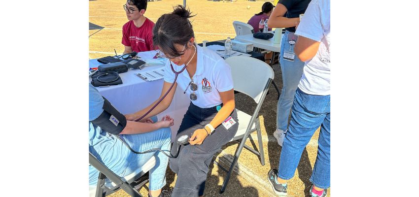 A person participating in an outdoor medical outreach event, seated at a table with supplies.