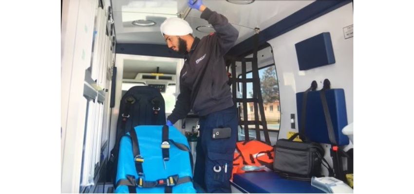 A paramedic in uniform inside an ambulance, adjusting equipment and preparing for use.