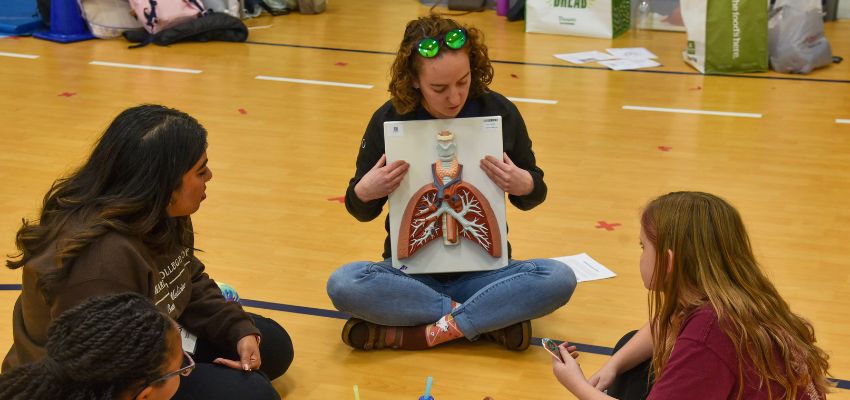 An instructor demonstrating a medical model to a group of young learners sitting on the floor.