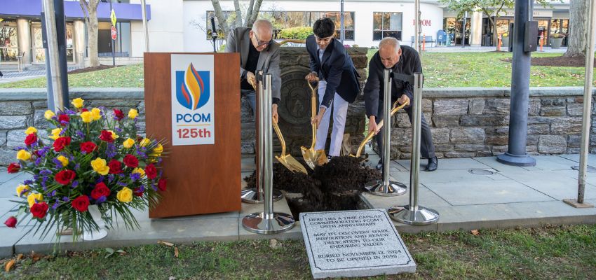 Three individuals break ground with golden shovels during a ceremony celebrating PCOM's 125th anniversary.